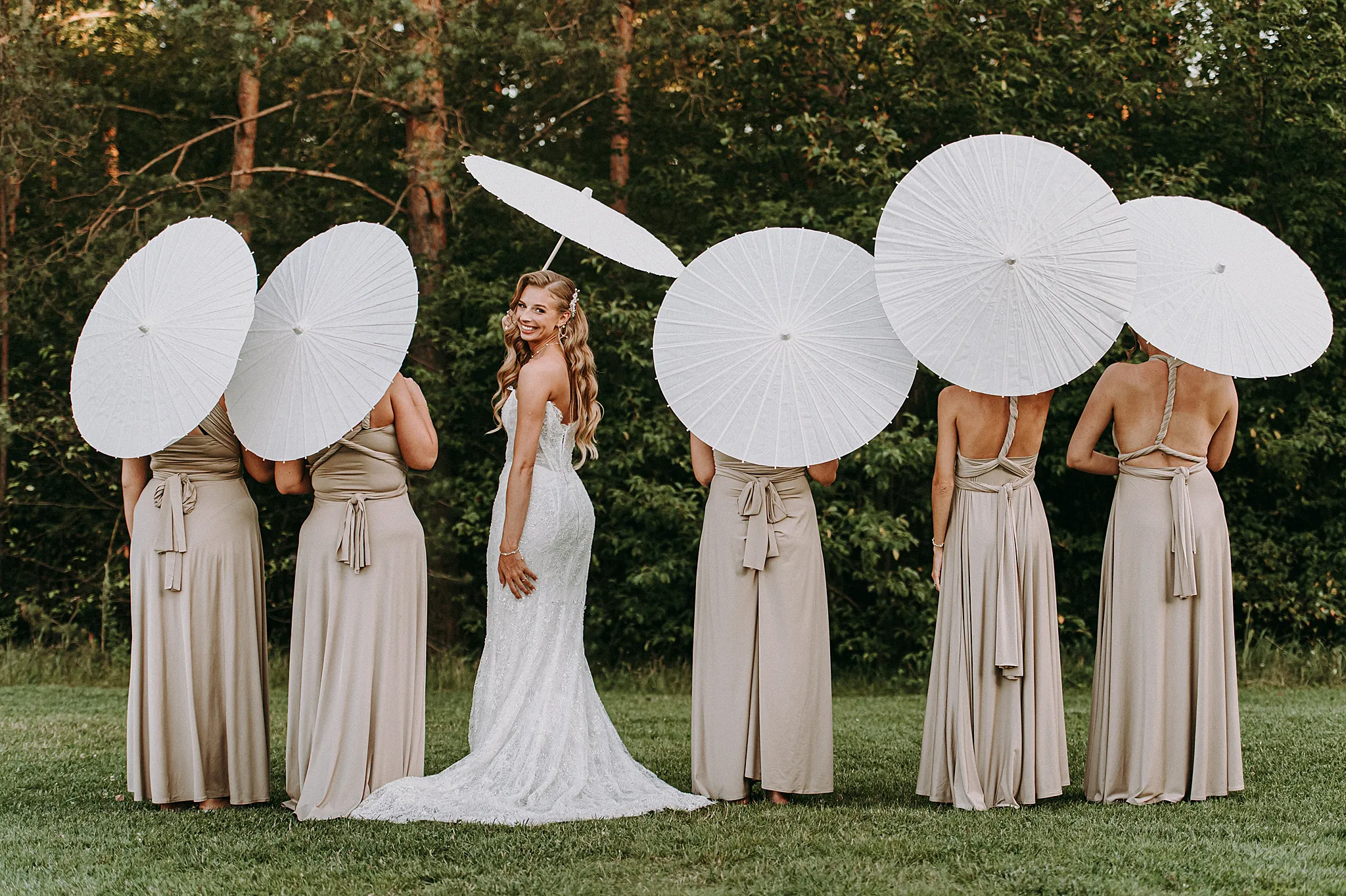 Panna młoda i jej druhny pozują z białymi parasolami, tworząc radosną i stylową kompozycję w słoneczny dzień.